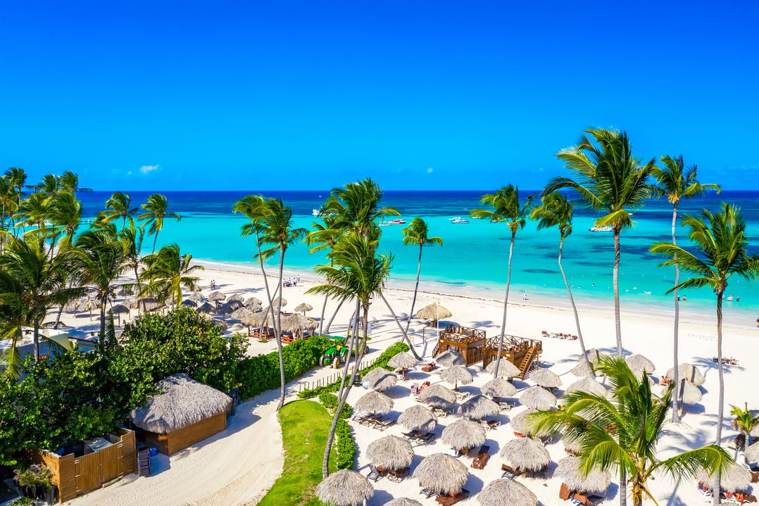 Aerial drone view of beautiful atlantic tropical beach with palms, straw umbrellas and boats. Bavaro, Punta Cana, Dominican Republic. Vacation background.